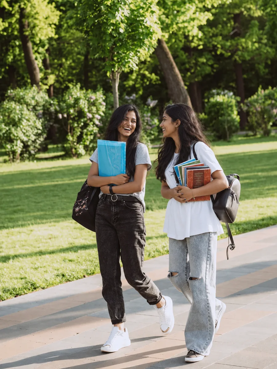 Two Indian students walking across a campus lawn with books